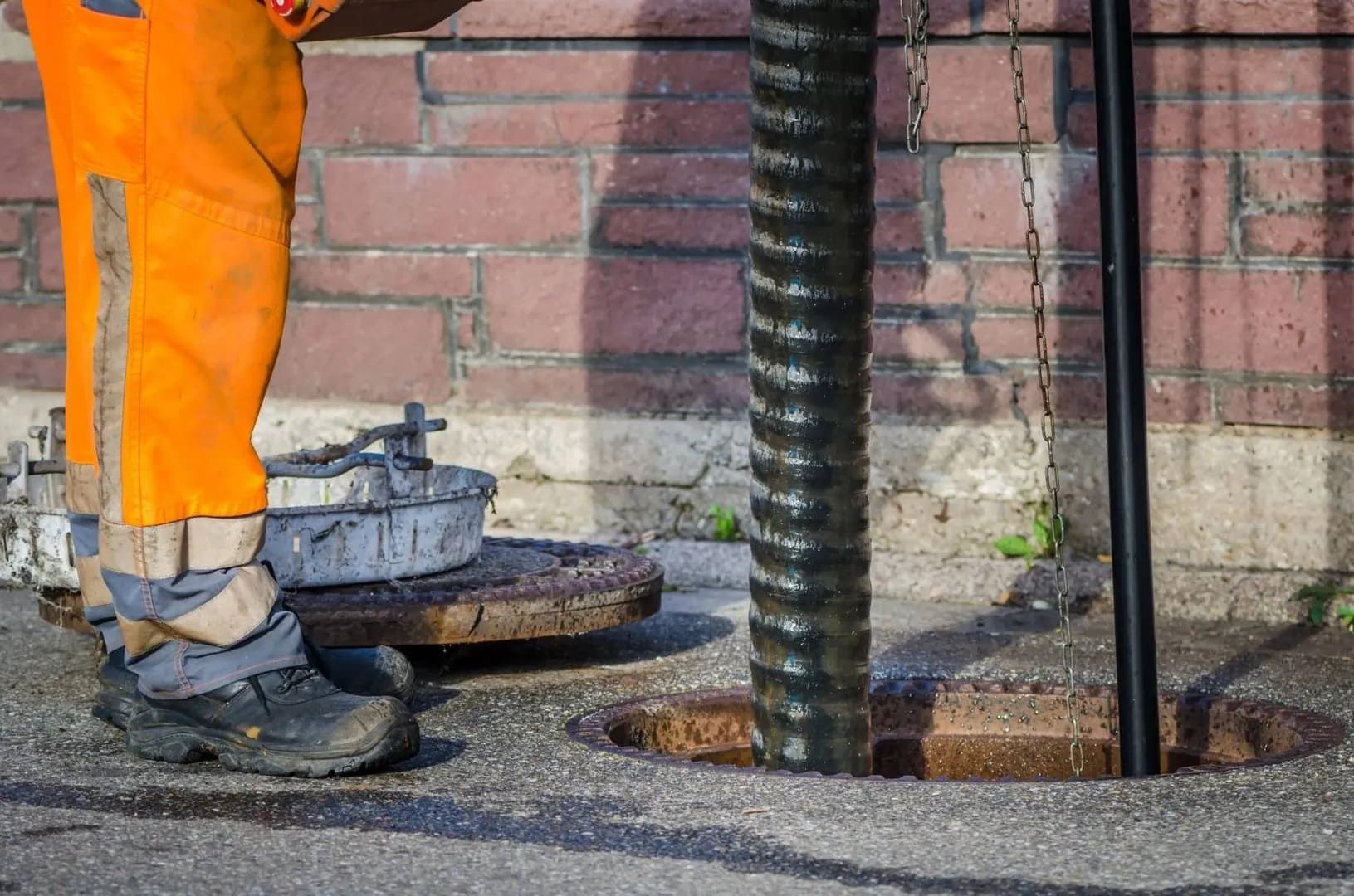 Mann in Sanitäroveralls steht neben einem Abflussdeckel